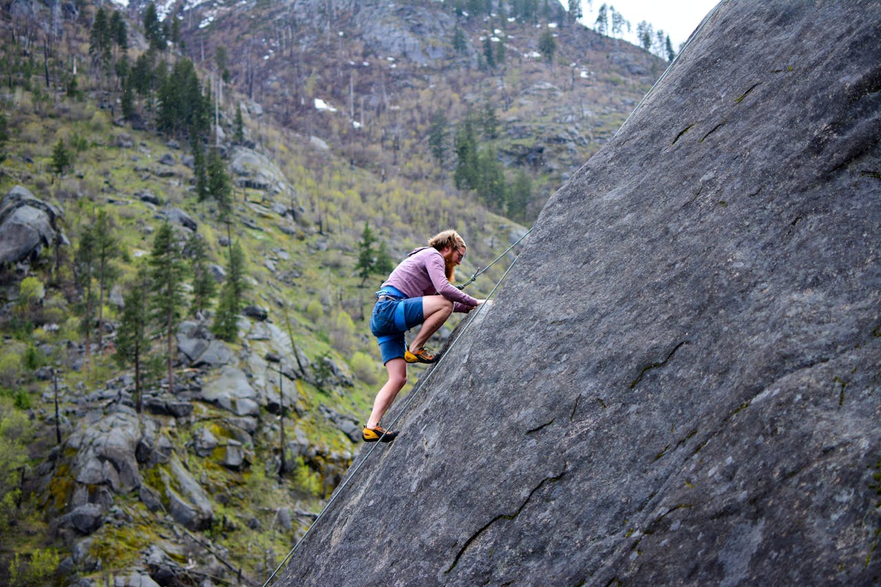 about-01 A climber in shorts skillfully ascends a steep rock face in a scenic mountainous environment.
